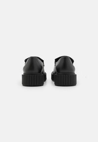 Scarpe di pelle nera con forma arrotondata, dotate di una suola in gomma nera rigata. Nessun lacci o decorazioni visibili. Design pulito e minimalista.