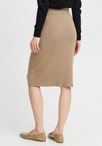 Jupe tricotée longueur genou en beige avec une texture côtelée. Taille et ourlet ajustés, assortie à des chaussures plates beiges. Fond blanc uni.