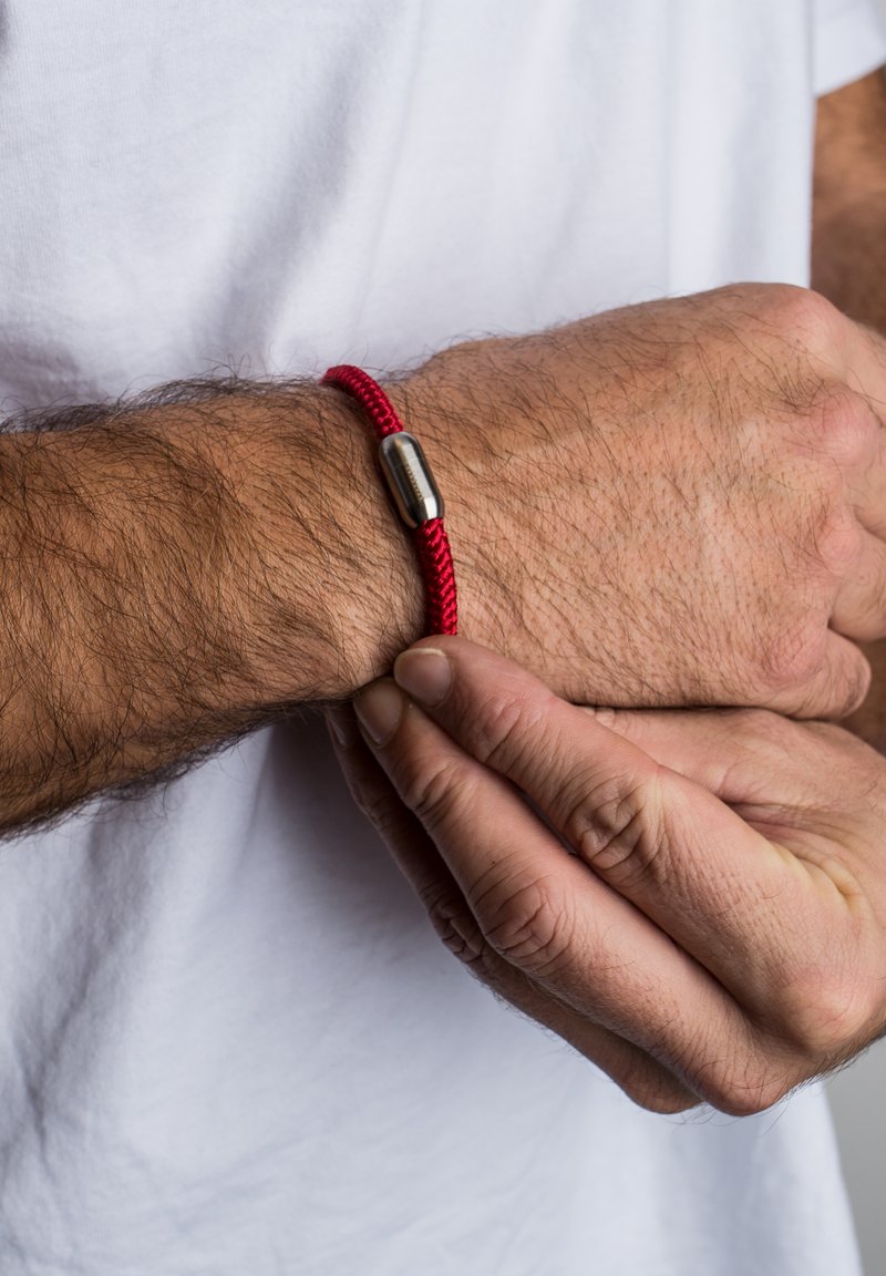 Punane palmikbracelet, millel on sile metallist lukustus, kantud randmel, kus on nähtavad juuksed, käed reguleerivad õrnalt bracelet'i.