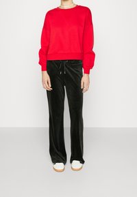 Sudadera roja recortada con mangas abullonadas, combinada con pantalones de velour negros con cordón. Zapatillas blancas con suelas beige completan el conjunto.