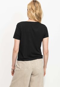 Haut noir à manches courtes côtelé avec un col arrondi. Porté avec un pantalon beige taille haute, montrant une coupe décontractée et une texture subtile.