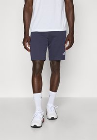 Calções de atletismo na cor azul-marinho, feitos de uma mistura macia de algodão. Apresentam um cós elástico e detalhes com o logótipo. Combinados com meias brancas e sapatilhas.