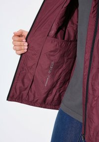 Burgunderfarbene leichte Jacke mit strukturiertem Innenfutter, ausgestattet mit einem wasserdichten Etikett, einem Reißverschluss und einer Innentasche.