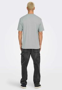 T-shirt grigio a maniche corte abbinato a pantaloni cargo scuri con più tasche. L'outfit ha una vestibilità comoda ed è realizzato in materiale di cotone.