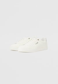 Vita sneakers gjorda av slät syntetiskt material, med en texturerad tåhuvud, perforerade detaljer på sidan och platta snören.