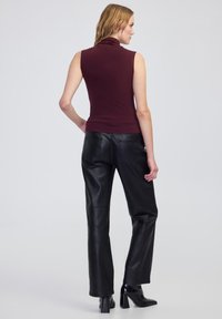 Bordeaux mouwloze coltrui gecombineerd met hoge zwarte leren broeken, met rechte benen en een gladde textuur.