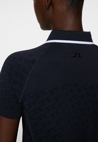 Marineblaues Polo-Shirt mit strukturiertem Muster, weißem Kragenakzent und schwarzem Logo auf dem Rücken, mit kurzen Ärmeln und taillierter Passform.