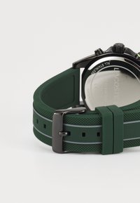 Montre avec un bracelet en silicone vert, un boîtier en métal noir poli, une surface texturée et des accents argentés. Résistante à l'eau avec un design élégant.