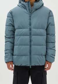 Vadderad jacka med huva i dämpad teal, med dragkedja framtill, elastiska ärmslut och ett kviltat mönster. Materialet verkar slätt med en svag lyster.