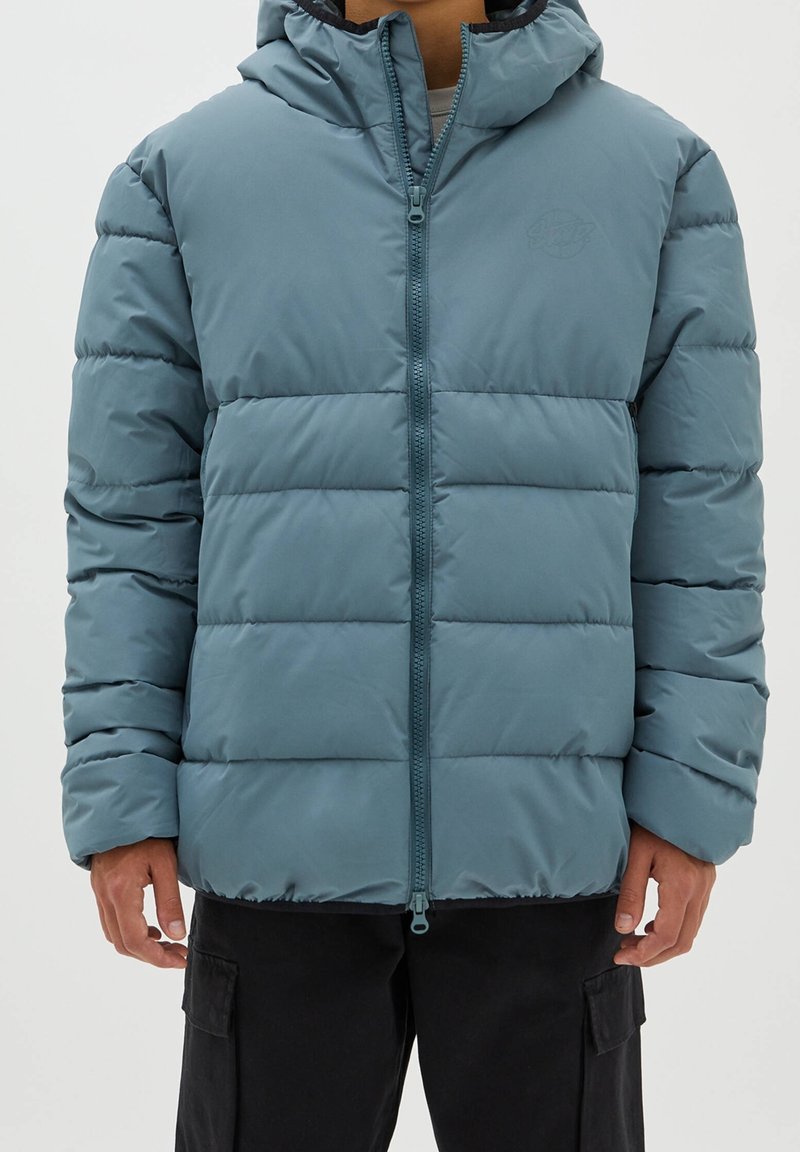 Vadderad jacka med huva i dämpad teal, med dragkedja framtill, elastiska ärmslut och ett kviltat mönster. Materialet verkar slätt med en svag lyster.