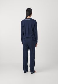 Conjunto de pijama azul-marinho feito de tecido macio, com mangas compridas, calças e detalhes brancos na gola e nos punhos. Textura suave.