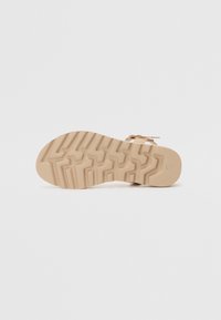 Lys beige gummisåle med et teksturert sikksakkmønster for grep. Har en minimalisk design og en glatt overflate.