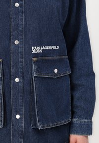 Jachetă din denim de culoare bleumarin închis, cu butoane tip snap, două buzunare frontale și logo-ul alb "KARL LAGERFELD JEANS" pe piept.