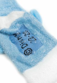 Calzini pelosi azzurri chiari con un polsino a coste bianche, caratterizzati da una toppa lavorata a maglia blu con testo nero e piccoli motivi a pois. Materiale morbido e strutturato.