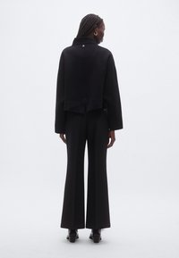 Sweat-shirt court noir avec un col montant et un détail subtil de boutons, associé à un pantalon large noir en texture lisse.