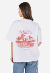 White oversized t-shirt featuring a red graphic design on the back with the word "Pegador" and a nature scene, short sleeves, and a crew neck.