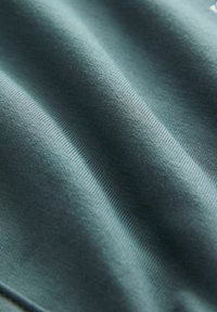 Türkisfarbener Baumwollstoff mit glatter Textur, der dezente gewebte Muster und unterschiedliche Schattierungen aufweist, was ein geripptes Erscheinungsbild erzeugt.
