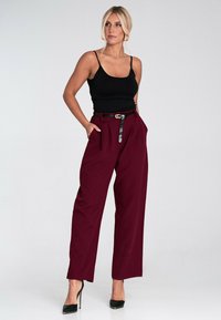Bordowe spodnie o szerokich nogawkach z czarnym paskiem z materiału sztucznego skóry i bocznymi kieszeniami, w zestawie z dopasowanym czarnym topem na ramiączkach i czarnymi szpilkami.