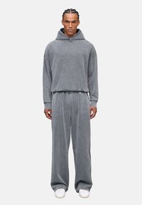 Grauer, oversized Hoodie und passende Jogginghose aus weichem, strukturiertem Stoff, mit einem gestickten Logo auf der Hose und einem lockeren Schnitt.