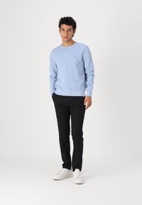 Lys blå genser med lange ermer og ribbestrikket kant, kombinert med svarte bukser og hvite joggesko. Diskret merkevare på brystet.