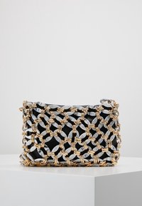 Czarna prostokątna kopertówka owinięta plecionką z łańcucha w złotych i marmurowo-szarych odcieniach, spoczywająca na białej powierzchni.