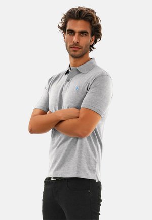 Graues Poloshirt mit Kragen, kurzen Ärmeln und blauem Emblem auf der Brust. Kombiniert mit schwarzen Hosen. Glatte Textur.