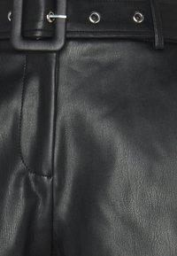 Los pantalones de cuero negro presentan una superficie texturizada, un cinturón ancho con una hebilla rectangular y accesorios de plata con detalles de costura visibles.