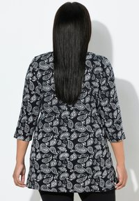 Schwarz-weiße Tunika mit Paisley-Muster und Dreiviertelärmeln, die eine lockere Passform und Seitenschlitze für Bewegungsfreiheit bietet.