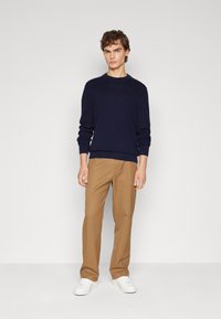 Maglione a maniche lunghe blu scuro con collo rotondo abbinato a pantaloni marrone chiaro e sneaker bianche. Il maglione presenta polsini e orlo a coste.