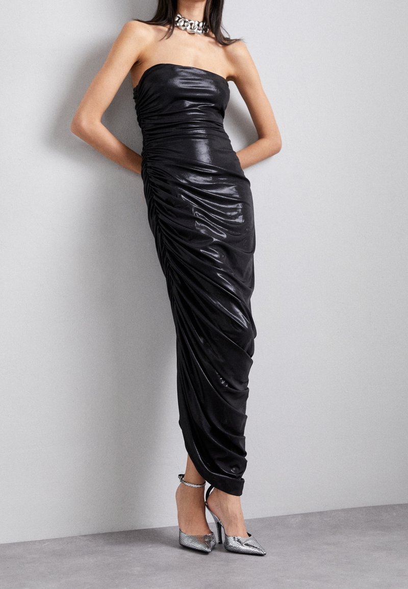 Černé bezramínkové šaty s nabíraným designem, hladkým povrchem a dlouhým střihem. V kombinaci s metalickými vysokými podpatky.