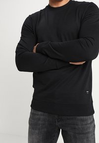 Felpa nera a maniche lunghe con colletto rotondo, realizzata in un tessuto liscio, caratterizzata da un design aderente e polsini e orlo a coste.