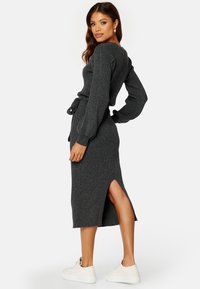 Dunkelgraues, geripptes Strickkleid mit langen Ärmeln, seitlichem Schlitz und einem Bindegürtel in der Taille, kombiniert mit weißen Sneakers.