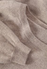Béžový pletený svetr s kulatým výstřihem, texturovanou látkou a žebrovanými manžetami s měkkým, mírně načechraným vzhledem.