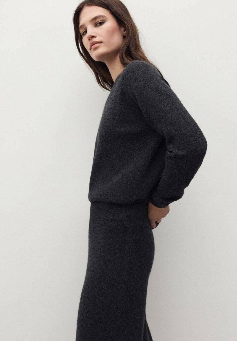 Maglione lavorato a maglia grigio scuro con maniche lunghe, abbinato a una gonna aderente coordinata. Texture morbida e design minimalista in profilo laterale.