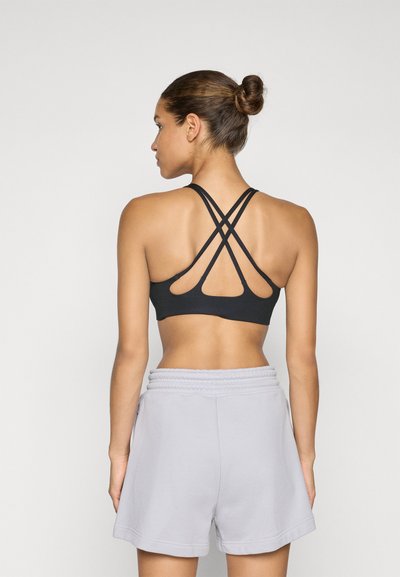 Μαύρο αθλητικό σουτιέν με σχέδιο σε σταυρό στην πλάτη, συνδυασμένο με ανοιχτό γκρι σορτς με ελαστική μέση. Λείο ύφασμα και μινιμαλιστικό στιλ.