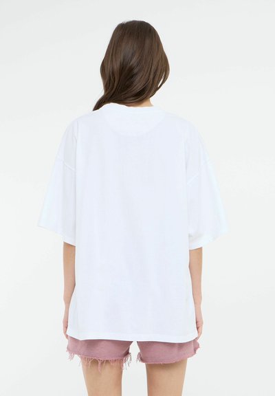 Hvit oversized T-skjorte med korte ermer, glatt tekstur og rund halsline, parret med rosa frynsete denimshorts.