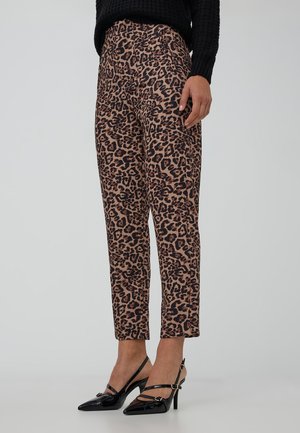 Donna che indossa pantaloni a sigaretta maculati marroni e neri e décolleté slingback in pelle lucida nera con fibbie.