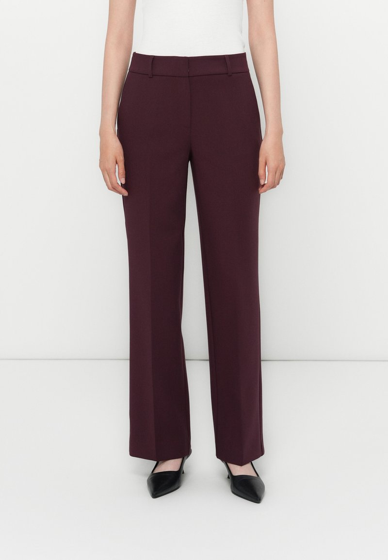 Pantalons larges bordeaux en tissu lisse, dotés d'une taille mi-haute et de plis discrets, associés à des chaussures noires à bout pointu.