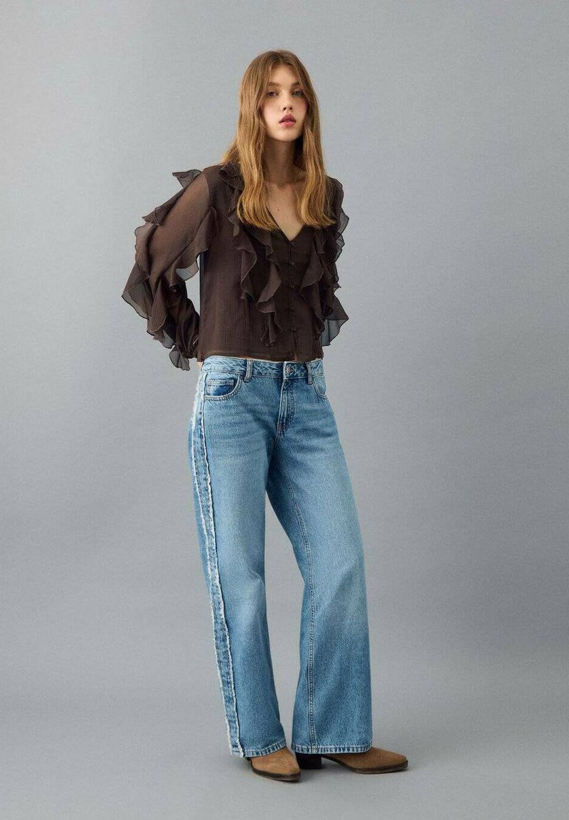 Černá halenka s nařasenými dlouhými rukávy, doplněná světle modrými džíny s širokými nohavicemi a bočními pruhy a světle hnědými kotníkovými botami.