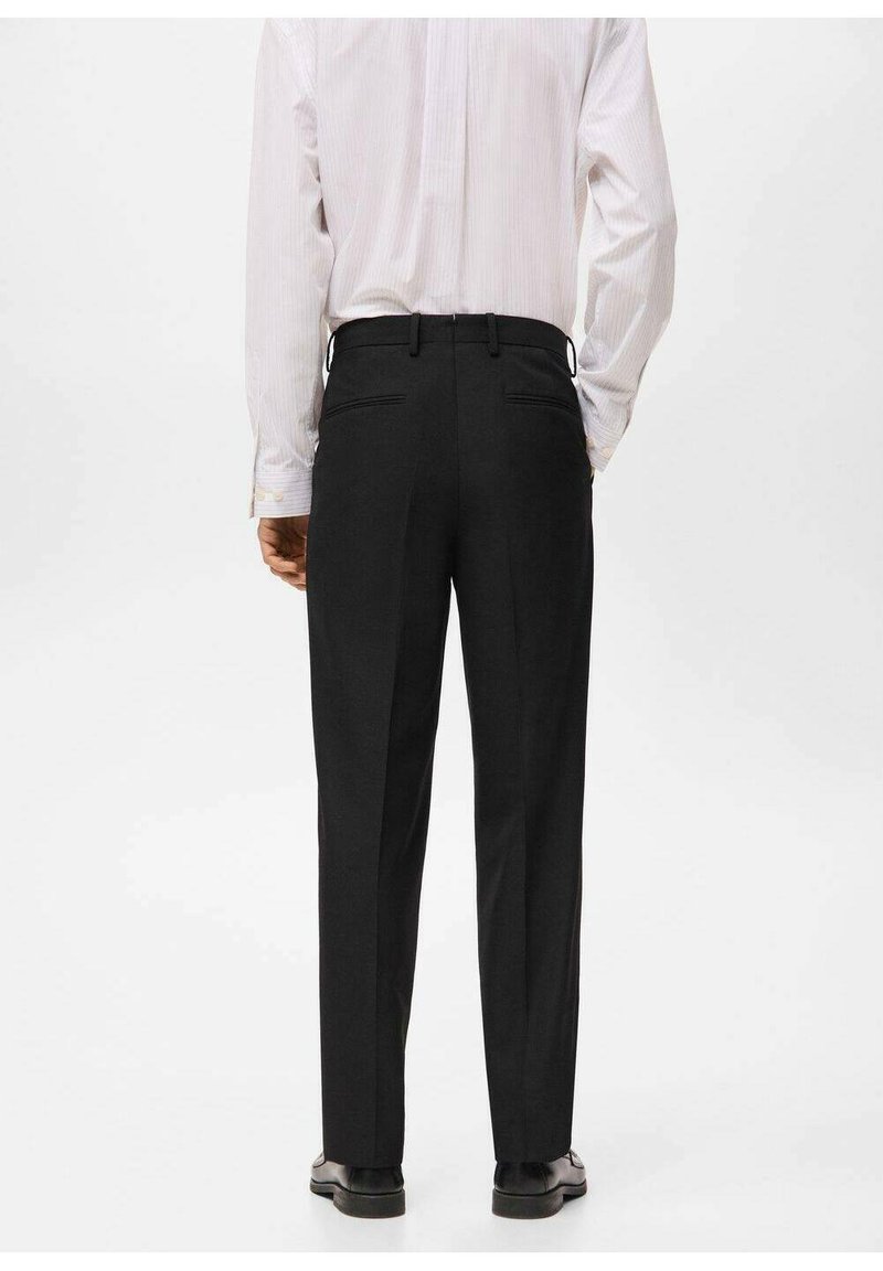 Schwarze maßgeschneiderte Hose im geraden Schnitt, mit zwei Gesäßtaschen und einer glatten Stofftextur. Getragen mit einem hellgestreiften Hemd.