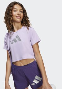 Top atletico corto viola con logo argento e pantaloni corti viola abbinati con accenti riflettenti. Tessuto morbido con vestibilità comoda.