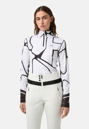 Haut à manches longues zippé en blanc avec un motif abstrait noir, associé à un pantalon blanc taille haute avec une bande d'accent noire et quincaillerie.