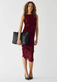 Burgundyröd figurnära klänning med blommönsterbroderi, semitransparent överlägg och rynkning. Matchad med en svart vävd handväska. Svarta klackar fulländar looken.