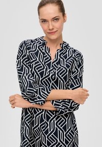 Marineblaues Kleid mit weißem geometrischem Muster, mit Kragen, dreiviertelärmeln und lässiger Passform. Leichter Stoff mit glatter Textur.