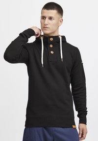 Felpa con cappuccio nera in cotone, dotata di una chiusura a bottoni con bottoni di legno, dettagli color sabbia a contrasto e particolari con cordoncino.