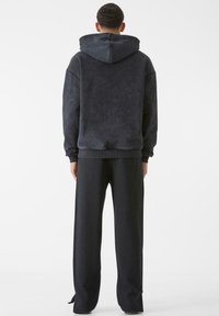 Tamsiai pilkas gobtuvėlis su laisvu kirpimu, pagamintas iš minkštos, tekstūruotos medžiagos, su elastingomis rankovėmis, derinamas su atitinkančiomis plačiomis kelnėmis.