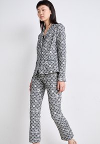 Grau gemusterter Anzug mit geometrischem Design, taillierter Blazer mit Reverskragen und schmal geschnittene Hose, alles aus glattem Stoff.