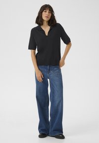 Zwarte polo met korte mouwen en een V-hals, gecombineerd met wijde blauwe jeans en chunky zwarte schoenen. Eenvoudig en minimalistisch ontwerp.