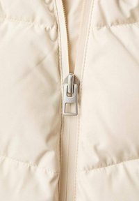 Crème puffer vest met een volledige rits en zilveren details, met doorgestikte secties en een gladde, licht glanzende textuur.