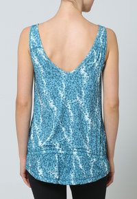 Débardeur bleu avec un dos échancré en V. Le tissu présente une finition brillante avec un motif géométrique dans différentes nuances de bleu.